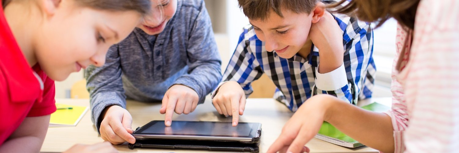 Zwei Mädchen und zwei Jungen beugen sich an einem Tisch über Tablets. 
