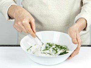 Eine Person verrührt Kräuter im Quark.