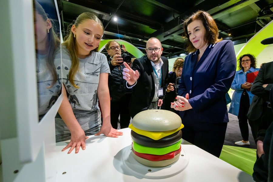 Besucher stehen an einem Ausstellungsexponat, der einen Hamburger darstellt.