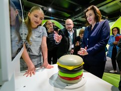 Besucher stehen an einem Ausstellungsexponat, der einen Hamburger darstellt.