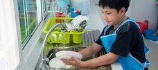 Junge mit Kochschürze spült Geschirr