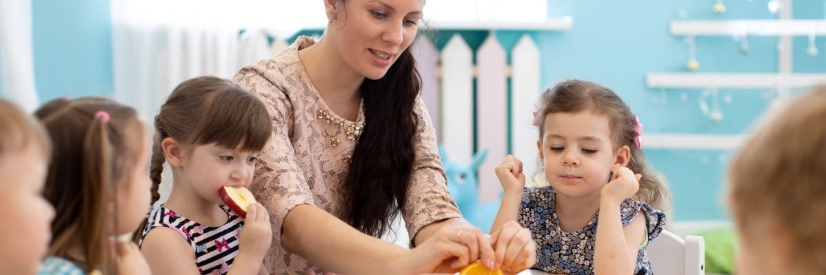 Kitakinder essen mit ihrer Erzieherin vorgeschnittene Orangen. 