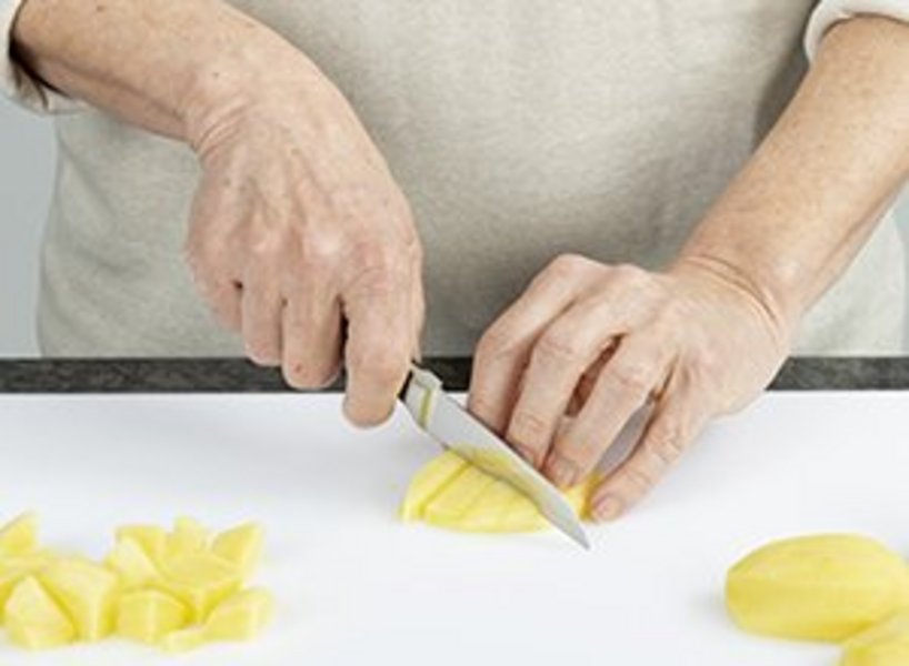 Person schneidet eine geschälte Kartoffel in kleine Würfel.