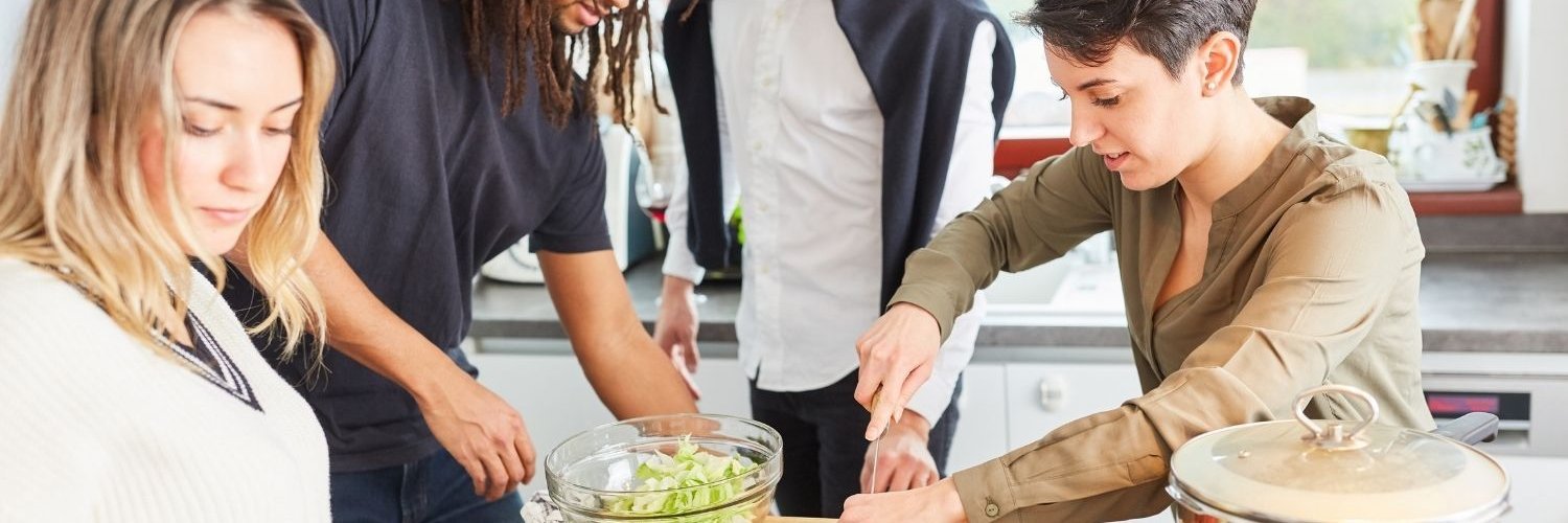 Vier junge Erwachsene bereiten in einer Küche zusammen Salat und Spaghetti zu.