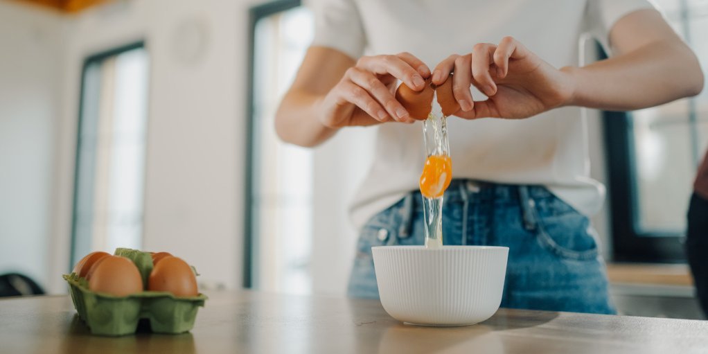 Frau schlägt Ei über einer Schüssel auf.
