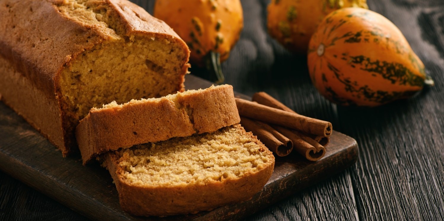 Auf einem dunklen Holztisch liegt ein kastenförmiges aufgeschnittenes Kürbisbrot, daneben Zimtstangen und Zierkürbisse.. Artikel "Herbstliche Kuchen backen" öffnen.