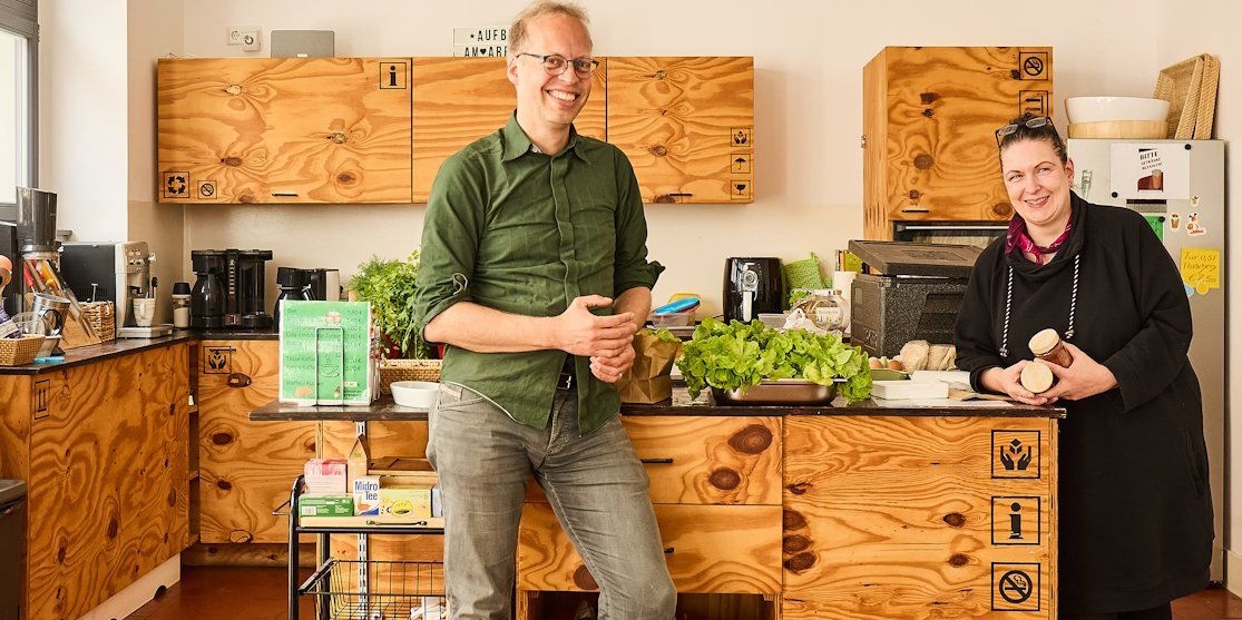 Ein Mann und eine Frau stehen in einer Kueche und laecheln in die Kamera.