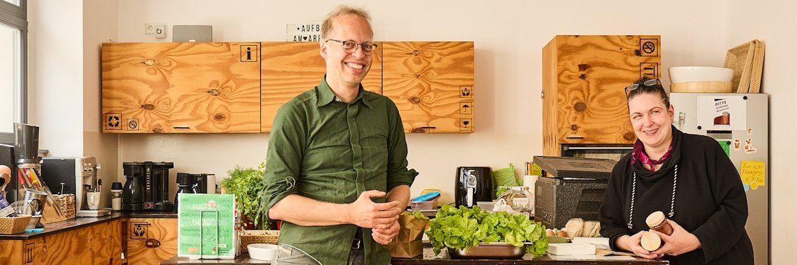 Ein Mann und eine Frau stehen in einer Kueche und laecheln in die Kamera.