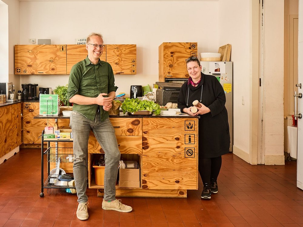 Ein Mann und eine Frau stehen in einer Kueche und laecheln in die Kamera.