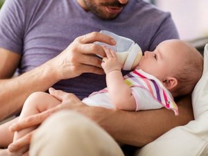 Ein Mann füttert ein Baby mit einer Flasche. 