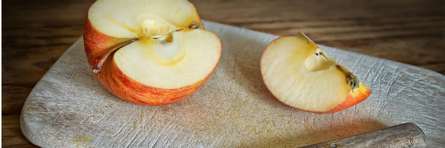 Auf einem Holzbrettchen liegen ein halber Apfel und ein Viertel, sowie ein Küchenmesser.