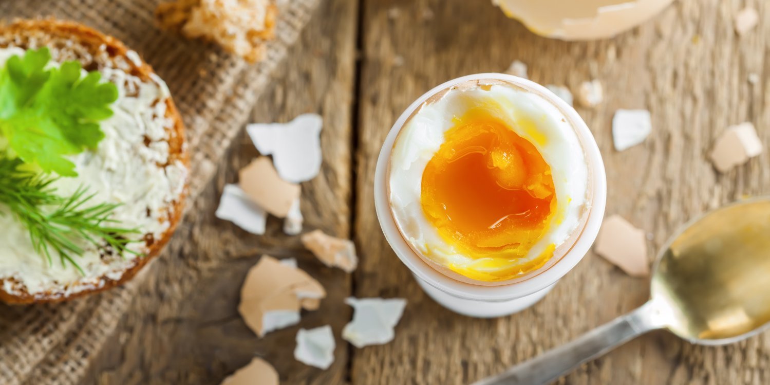 Waxhsweich gekochtes Ei steht geöffnet inn einem Eierbecher auf einem Holztisch.. Artikel "Eier: Gesundheit und Umwelt" öffnen.