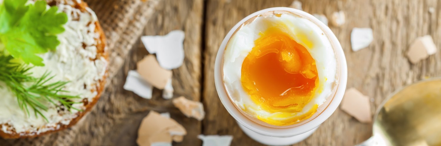 Waxhsweich gekochtes Ei steht geöffnet inn einem Eierbecher auf einem Holztisch.