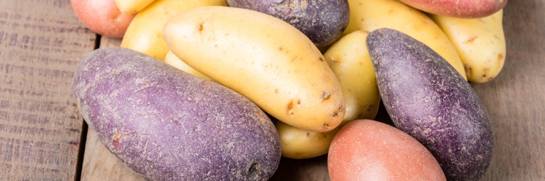 Bunte Kartoffelsorten liegen auf einem Holztisch.