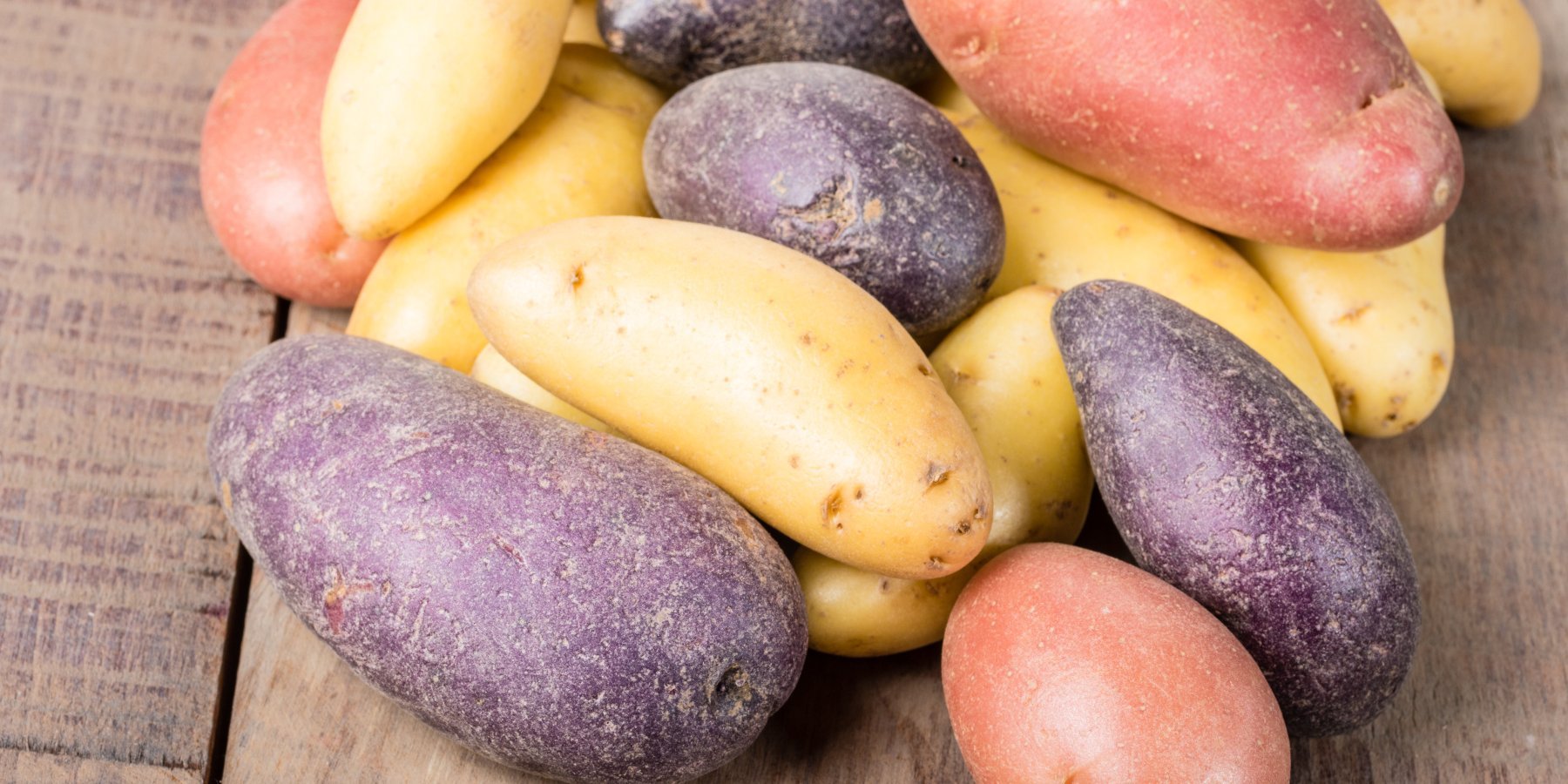 Bunte Kartoffelsorten liegen auf einem Holztisch.. Artikel "Kartoffeln" öffnen.