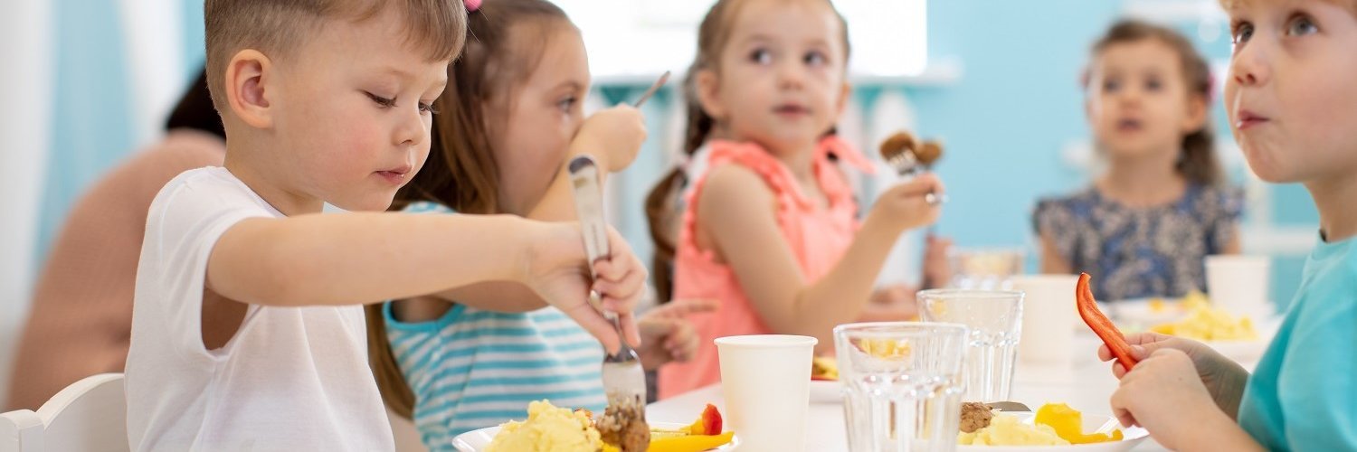 Eine Gruppe von Kindergartenkindern sitzt am Tisch und isst gemeinsam. 