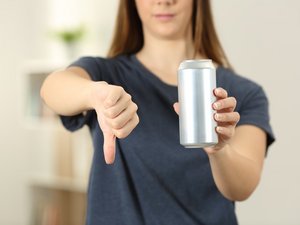 Eine Frau mit Energy-Drink zeigt mit dem Daumen nach unten.