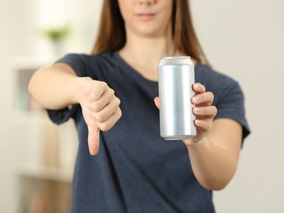 Eine Frau mit Energy-Drink zeigt mit dem Daumen nach unten.