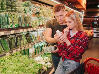 Ein Mann und eine Frau stehen im Supermarkt und lesen die Zutaten auf einer Salatdressing-Flasche