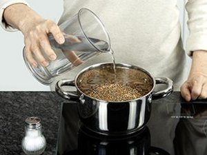 Person gießt Wasser in einen Kochtopf.