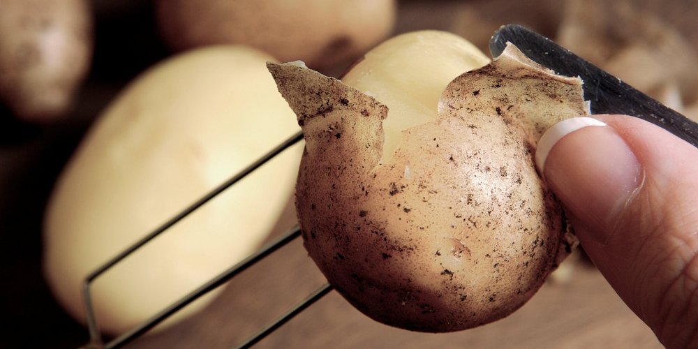 Von einer gekochten Kartoffel wird die Schale mit einem kleinen Küchenmesser abgezogen.