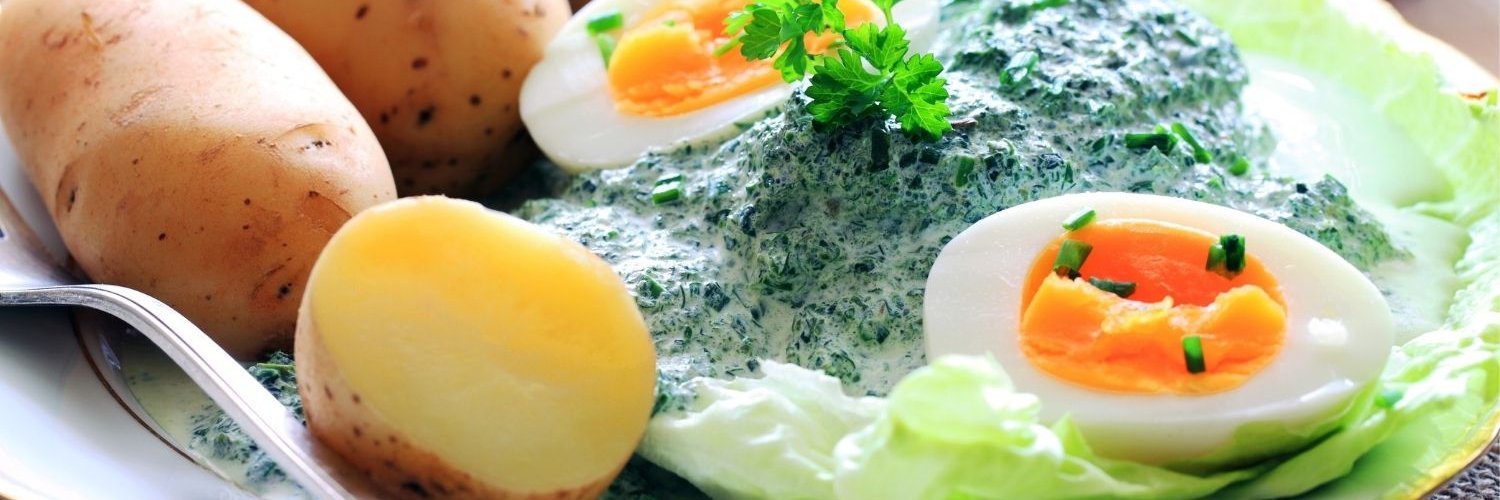 Auf einem weißen Teller sind Pellkartoffeln, hartgekochte Eier mit grüner Soße und Salatblätter angerichtet.