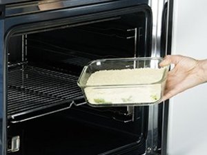 Eine Person schiebt Rhabarber-Crumble in Ofen.