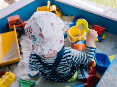 Baby sitzt mit Sonnenhut im Sandkasten uns spielt.