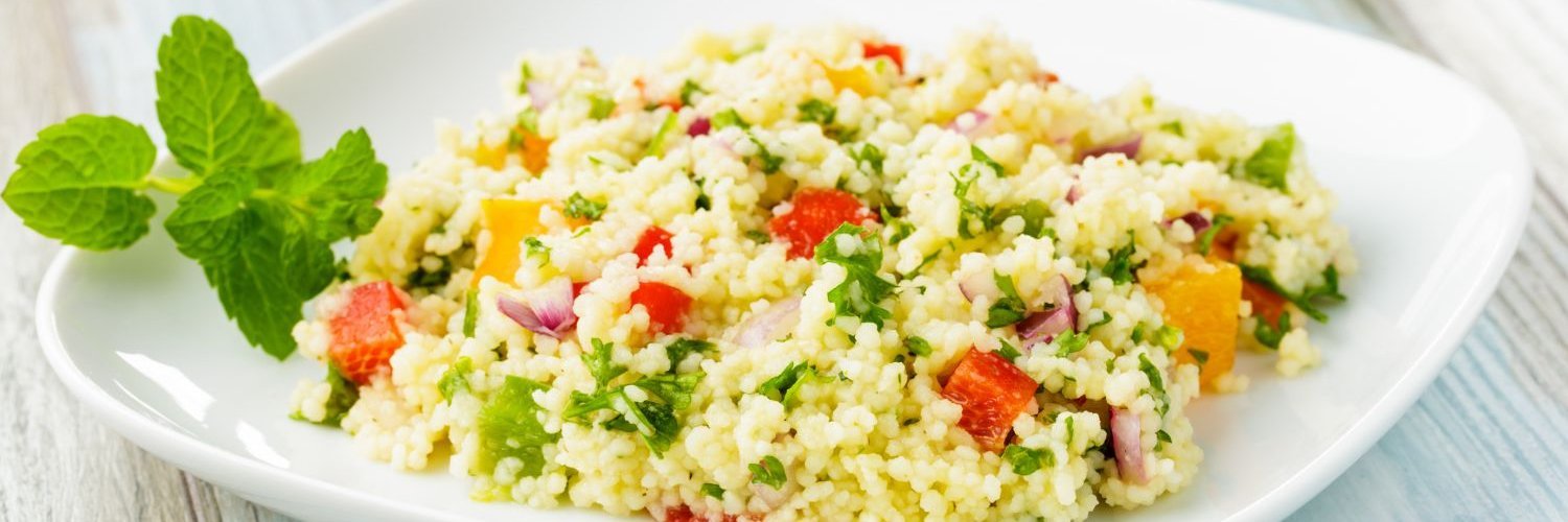 Auf einem weißen Teller befindet sich eine Portion Couscous-Salat mit roter und gelber Paprika, Lauch und Kräutern.