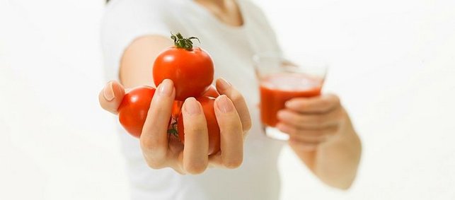 Eine Hand hält Tomaten und eine ein Glas mit Tomatensaft