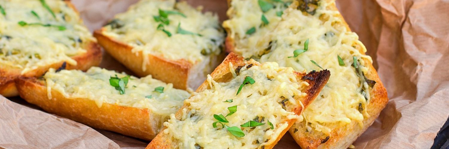 Auf Backpapier liegen Baguettestücke, mit Käse überbacken und mit Kräutern bestreut.