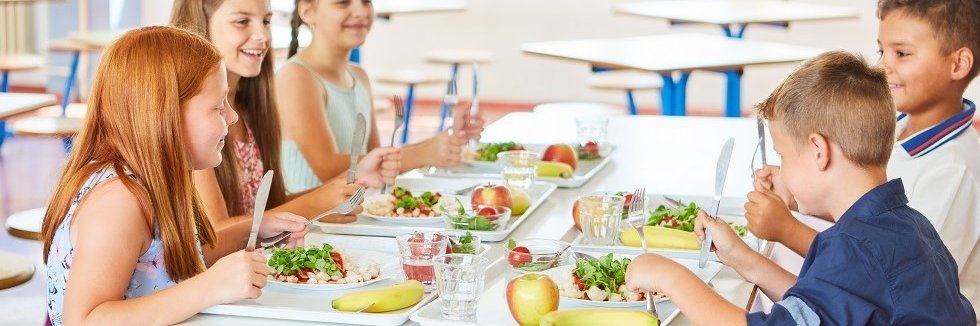 Zwei Jungen und drei Mädchen sitzen fröhlich an einem Tisch in der Mensa und essen gemeinsam ihr Mittagessen.