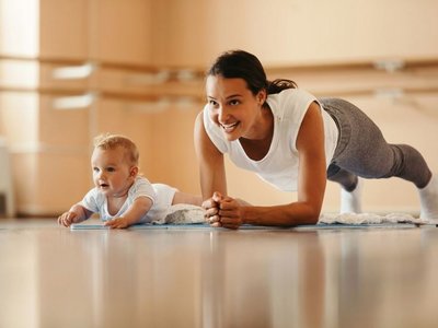 Eine Mutter macht Sport. Ihr Baby liegt neben ihr.