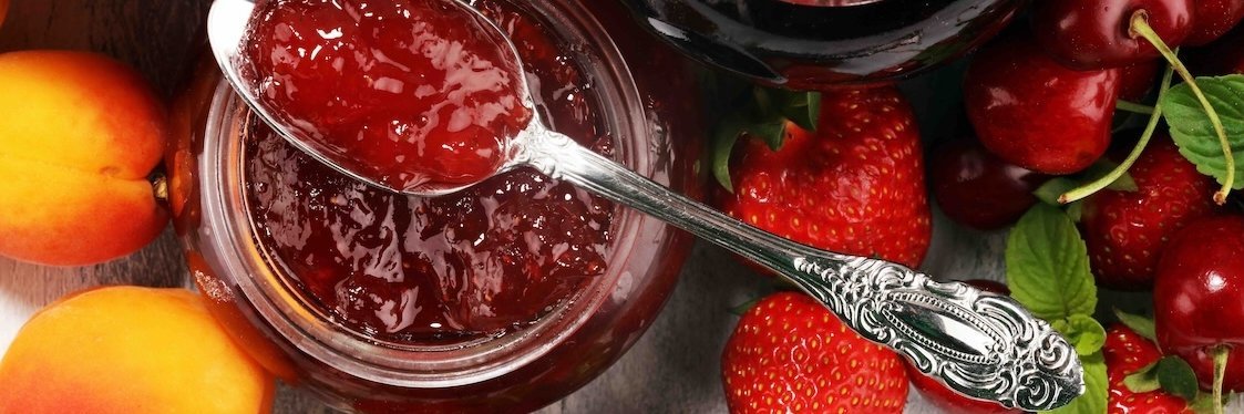 Geöffnete Marmeladengläser in einem appetitlichen Ambiente mit frischen Früchten.