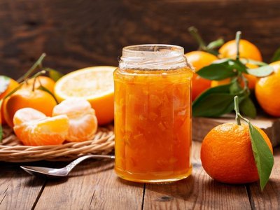 Ein appetitlich angerichtetes, geöffnetes Glas Mandarinenmarmelade mit frischen Früchten drumherum.