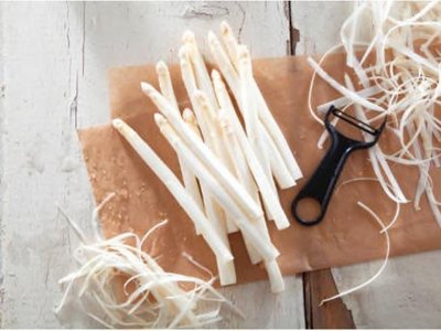 Frisch geschälter Spargel mit Schalen und Sparschäler auf einem Holzbrett.