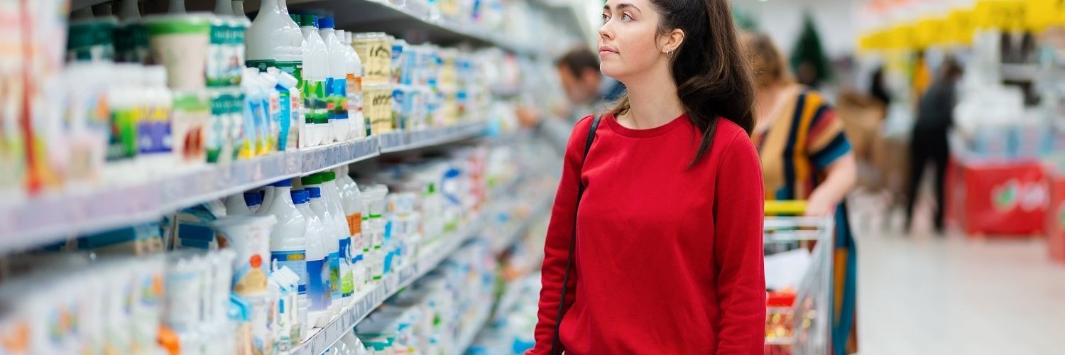 Eine junge Frau steht im Supermarkt vor einem Regal voller Lebensmittel. 