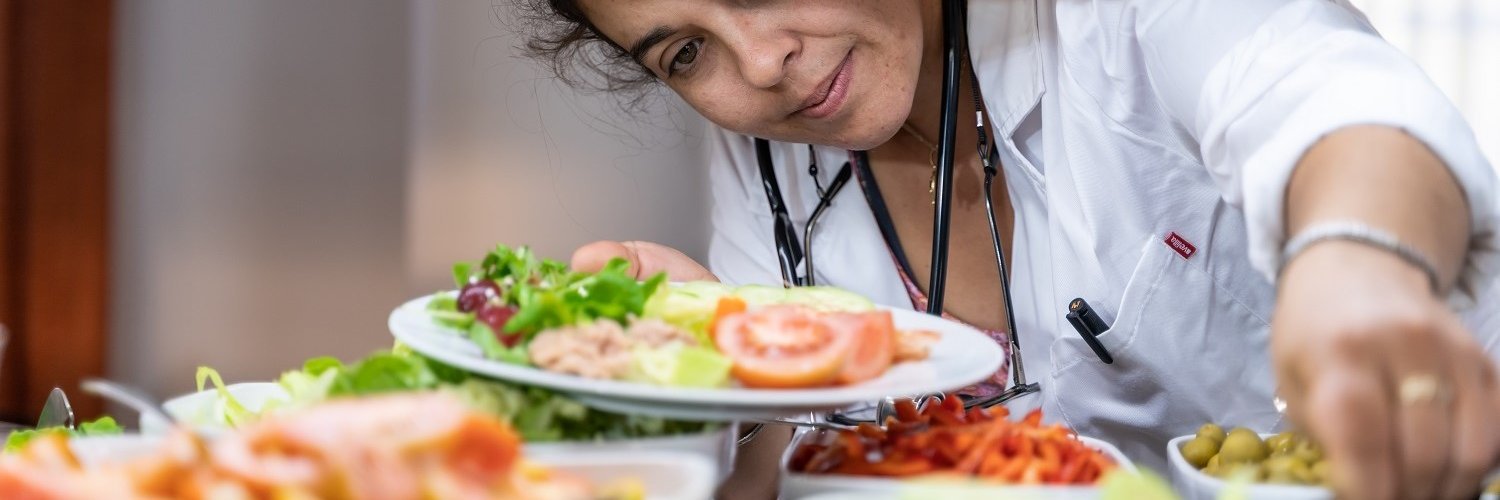 Eine Ärztin steht vor dem Salatbuffet in der Kantine und befüllt ihren Teller mit verschiedenen Salaten. 