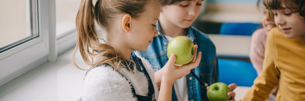 Drei Schulkinder sehen sich grüne Äpfel an.