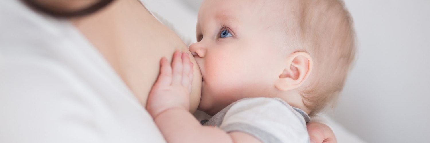 Ein älterer Säugling trinkt an der Brust und schaut zur Mutter auf.