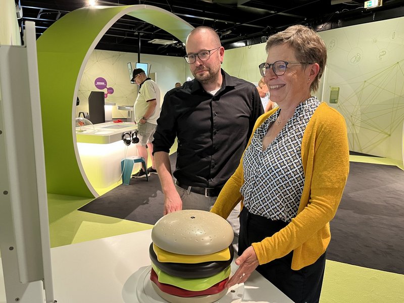 Barbara Kaiser und Lars Winterberg vom BZfE an einem Ausstellungsexponat, der einen Hamburger darstellt.