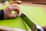 Kochmesser zerteilt Zwiebel auf grünem Schneidbrett quer in kleine Würfel. Hand hält die Zwiebel um den Strunk dabei im Krallengriff.