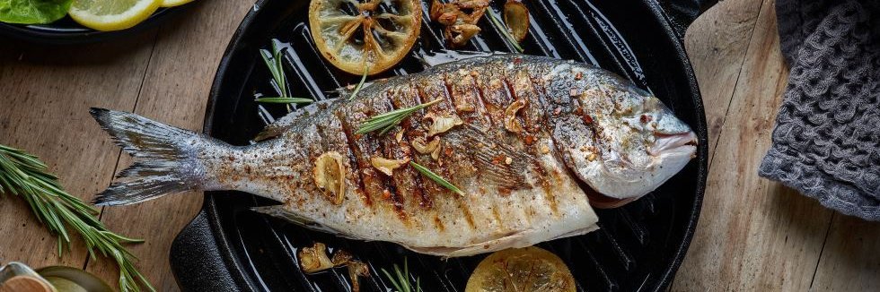 Ein ganzer Fisch liegt fertig zubereitet in einer Grillpfanne.