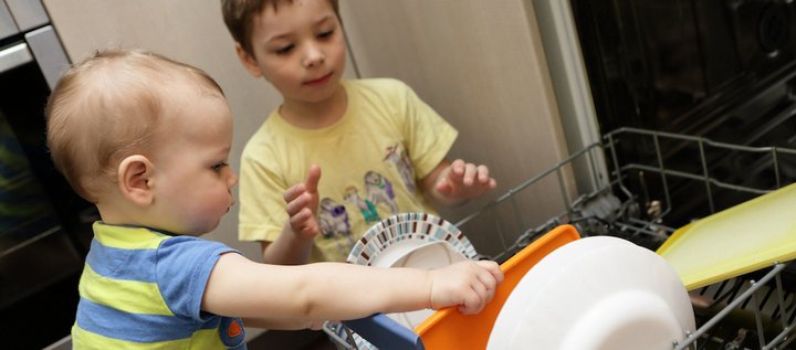 Zwei Kleinkinder räumen die Spülmaschine aus