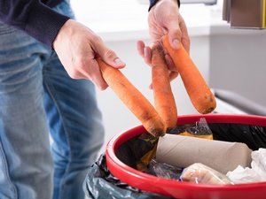 Eine Person wirft Karotten in den Mülleimer.