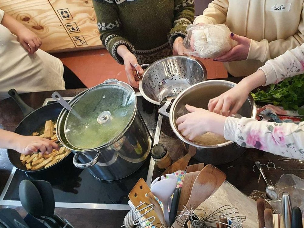 Mehrere Menschen stehen um Toepfe herum und hantieren mit ihren Haenden.