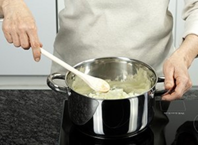 eine Person dünstet Zwiebelwürfel.