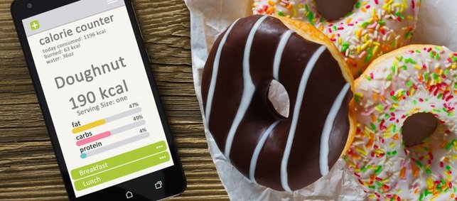 rechts liegen drei Donuts, auf der linken Seite ein Handy, auf welchem in einer App die entsprechenden Kalorien angezeigt werden