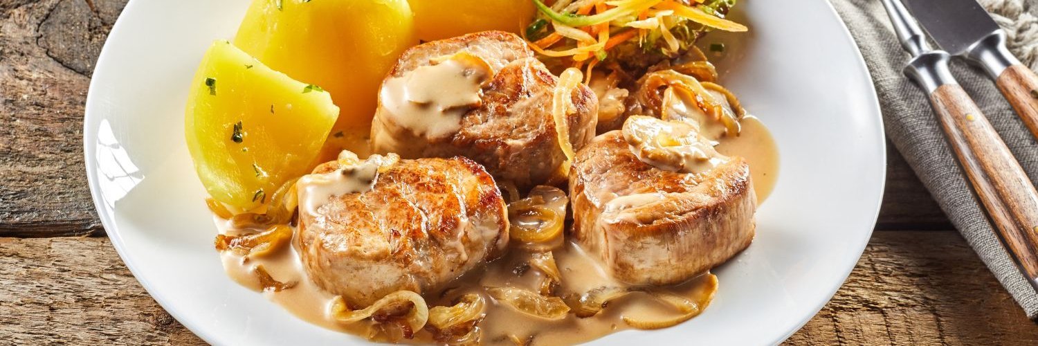 Auf einem weißen Teller liegen drei Stücke Schweinefilet mit einer Zwiebelsoße und Kartoffeln.