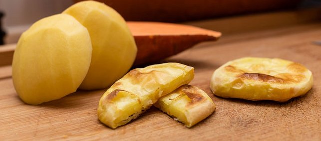 Getoastete Kartoffelscheiben neben roher Kartoffel und Süßkartoffel.
